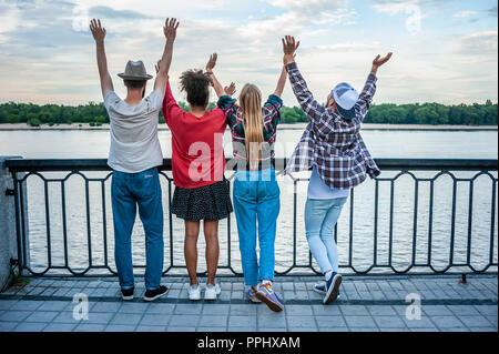 Vue arrière de quatre amis multiethnique sensibilisation mains à riverbank Banque D'Images