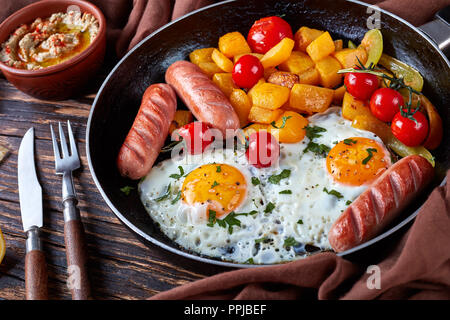 Repas du matin : de délicieux œufs frits, courge rôtie, tomates et saucisses, parsemé de feuilles de persil, sur une table en bois avec baba ganous Banque D'Images