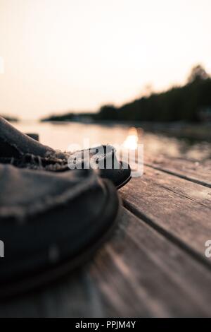 Une paire de chaussures d'été occasionnels de prendre une pause de leur vie difficile et le niveau de la semelle par appui sur un quai au coucher du soleil. Banque D'Images