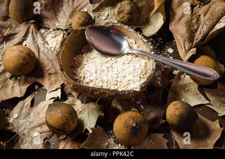 Plat de gruau servi au milieu d'une noix de coco à sec, garnie de citrons séchés et jaunâtres, de feuilles séchées sur un fond brun. Banque D'Images