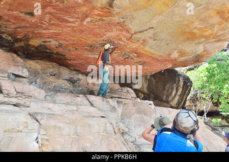 Guide autochtone soulignant artwork dans un rock art gallery sur Injalak Hill, la terre d'Arnhem, dans le Territoire du Nord, Australie Banque D'Images