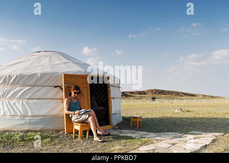 Une jeune femme est assise en face d'un ger mongole dans le désert de Gobi et est en train de lire un livre, la Mongolie Banque D'Images