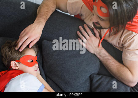 Portrait du père en rouge costume de super-héro à fils à dormir sur un canapé à la maison Banque D'Images