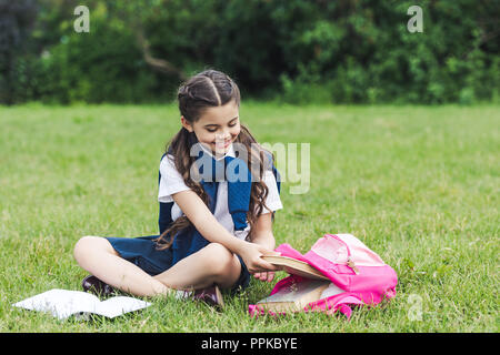 Belle lycéenne en tenant livre de sac à dos sitting on grass in park Banque D'Images