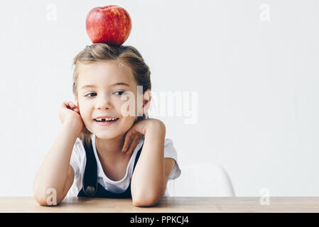 Petite lycéenne assis à table avec pomme rouge isolé sur blanc sur la tête Banque D'Images