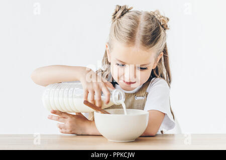 Happy little schoolgirl verser le lait dans les céréales pour le petit-déjeuner isolated on white Banque D'Images