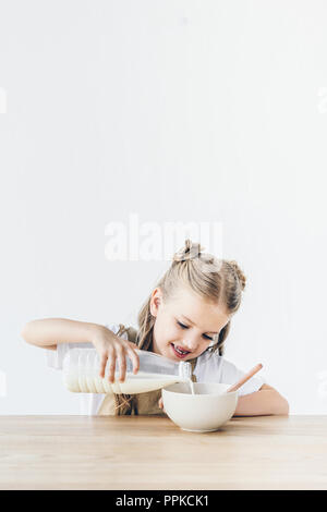 Smiling little schoolgirl verser le lait dans les céréales pour le petit-déjeuner isolated on white Banque D'Images