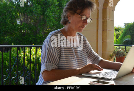 Femme assise à une table en bois sur une terrasse, à l'aide d'un ordinateur portable. Travailler de la maison en été. Banque D'Images