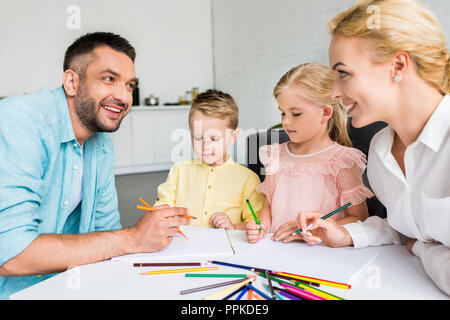 Heureux parents de deux petits enfants dessin avec des crayons de couleur à la maison Banque D'Images