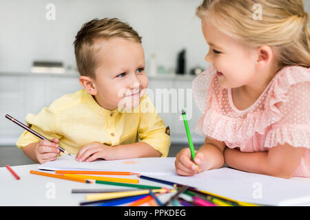 Adorable Kids smiling les uns les autres pendant le dessin avec des crayons ensemble Banque D'Images