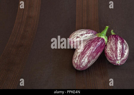 Aubergines bio frais sur toile sombre arrière-plan. Variété de légumes l'étrange appelé zebra, rayé ou sicilien. Copie espace gauche. Banque D'Images