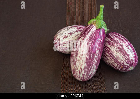Aubergines bio frais sur toile sombre arrière-plan. Variété de légumes l'étrange appelé zebra, rayé ou sicilien. Copie espace gauche. Banque D'Images