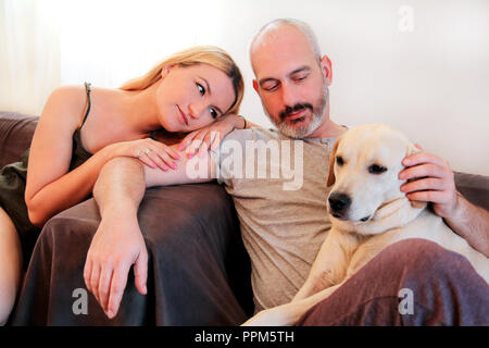 Deux personnes avec chien à la maison. Heureux les amoureux et mignon beau couple profiter avec leur chien labrador retriever jaune à chambre salon. Beau chien, Banque D'Images
