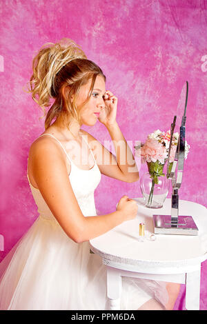 Teen girl préparer pour partie isolé sur fond blanc ou rose assis à table de maquillage appliquant le maquillage. Banque D'Images