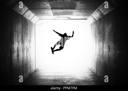 BW image en noir et blanc d'un seul étudiant de l'école se profilant sauter de haut et en cliquant sur leurs talons dans un tunnel. en direction de la lumière, l'obtention du diplôme Banque D'Images