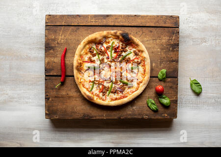 Une pizza boeuf haché avec des feuilles de basilic, tomates et un poivron rouge sur une surface en bois vintage Banque D'Images