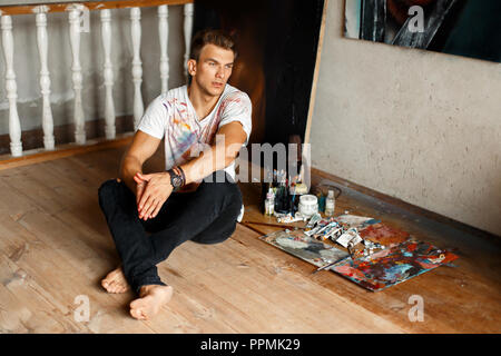 Bel homme jeune artiste dans un livre blanc shirt créatif assis sur le plancher dans le studio Banque D'Images