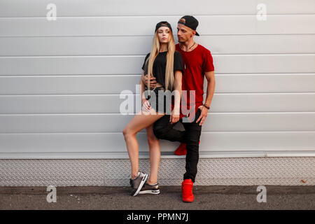 Beau jeune couple élégant dans le quartier chic des vêtements décontractés avec un stand de près d'un mur dans la rue Banque D'Images