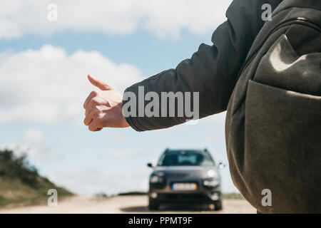 Close-up of a man randonneur avec un sac à dos de l'autostop. Il leva son doigt vers le haut et a essayé d'arrêter la voiture pour poursuivre son voyage. Banque D'Images