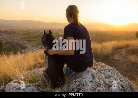 Husky de Sibérie et femme assise sur un rocher et regarder le coucher de soleil depuis un sommet Banque D'Images