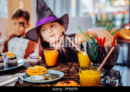 Assistant Girl wearing hat pour Halloween boire du jus et manger des bonbons gommeux Banque D'Images