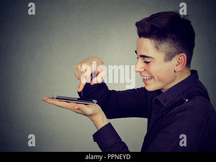 Side view of young man using smartphone heureux et souriant sur fond gris Banque D'Images