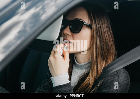 Cute young girl peintures pilote lèvres à l'intérieur de la voiture. Banque D'Images