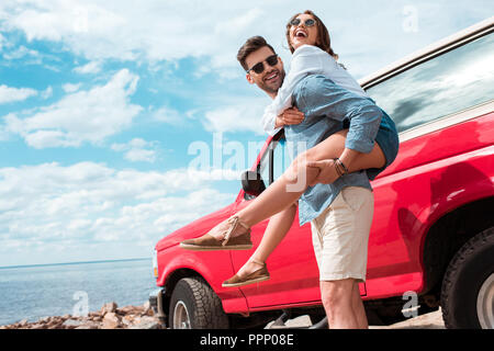 Jeune homme usurpation de son amie excité près de jeep rouge Banque D'Images