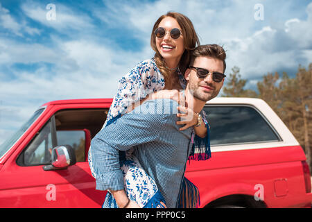 Young smiling couple en jumelant les lunettes près de voiture rouge Banque D'Images