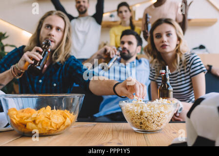 Young man drinking beer et prendre du popcorn de la cuvette au cours de regarder des match de foot avec les amis à la maison Banque D'Images