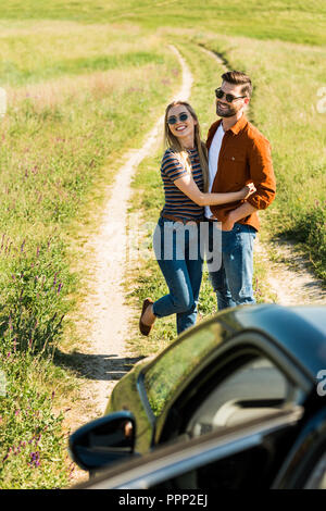 High angle view of young couple embracing lunettes élégant dans près de voiture sur meadow rural Banque D'Images