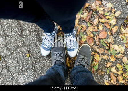 Vue d'en haut aux pieds de l'homme et de la femme debout entre les feuilles d'automne séchées ou à l'automne dans une perspective à la première personne. Banque D'Images