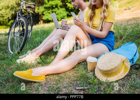 Vue partielle de couple avec ordinateur portable et smartphone resting on Green grass in park Banque D'Images