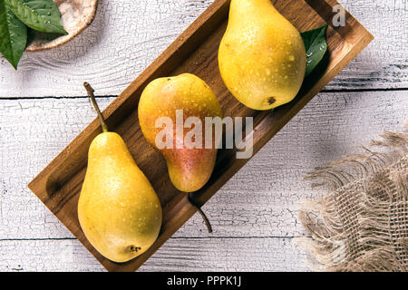 Poires jaunes avec des feuilles couvertes par les gouttes d'eau sur la plaque de bambou carré blanc sur la vieille table en bois avec des serviettes de toile d'un côté. Focus sélectif. Vi Banque D'Images