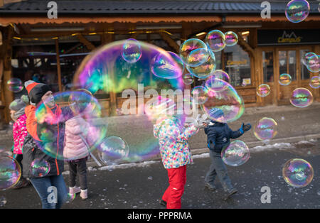 Karpacz, Pologne - Février 2018 : les enfants d'essayer d'attraper les bulles de savon géantes dans la rue principale à Karpacz ville, station de ski d'hiver polonais Banque D'Images