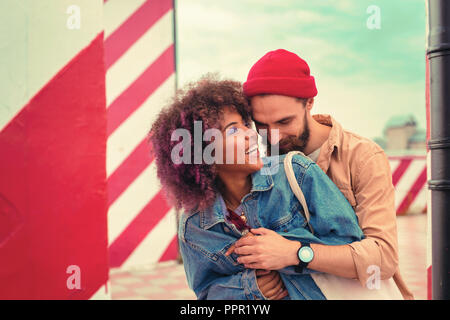 Jeune homme barbu debout derrière sa belle petite amie et l'étreindre Banque D'Images