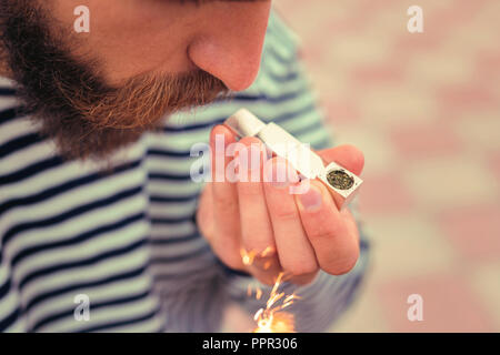 Jeune homme barbu en utilisant le briquet pour allumer sa pipe Banque D'Images