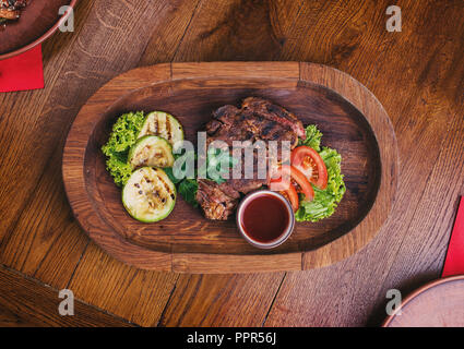 Sex steak avec tomates, salade, courgette, verts et de la sauce sur une planche de bois. Des en-cas pour la bière au pub Banque D'Images