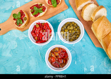 Crostini ou Bruschetta aux tomates séchées et câpres sur un conseil cuisine en bois avec fond bleu. Sandwiches italien frais.en-cas délicieux et Banque D'Images