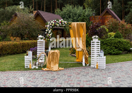 Arche de bois floral avec un chiffon jaune et des fleurs blanches avec des feuilles vertes sur une cérémonie de mariage rustique. Banque D'Images