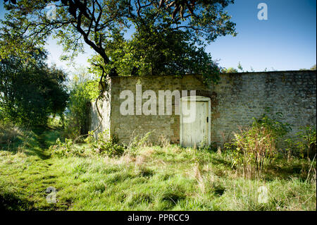 Une porte dans un mur, entouré d'arbres, l'herbe et les buissons à Sutton Veny, Wiltshire, Royaume-Uni. Banque D'Images