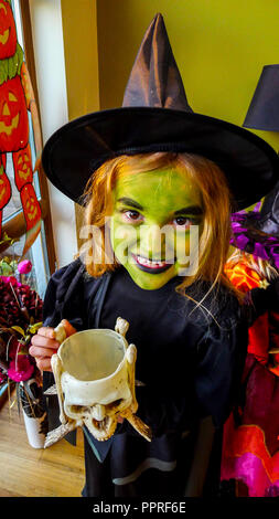 Petite fille avec un visage vert, la peinture pour le visage, vêtu d'un costume d'Halloween pour enfants, portant un chapeau de sorcière noir et robe noire. Banque D'Images