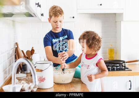 Frère et soeur de la préparation de la pâte à crêpes à la cuisine. Concept de préparation des repas, cuisine blanche sur l'arrière-plan. Serie photo style décontracté Banque D'Images