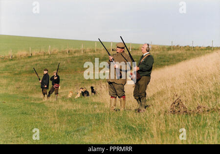 Un homme avec son fusil de chasse fume une pipe et attend patiemment pour faisans de survoler un champ de Wiltshire en Angleterre 2001. Banque D'Images