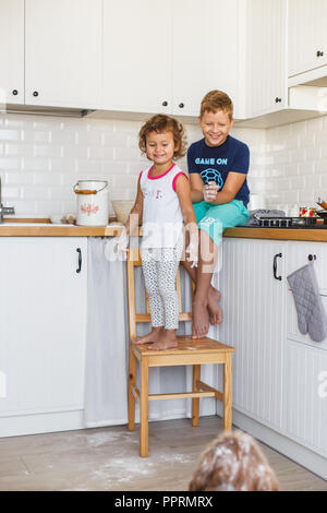 Frère et soeur de la préparation de la pâte à crêpes à la cuisine et jouer avec le chien. Style de vie décontracté de la série de photos d'intérieur dans la vie réelle Banque D'Images