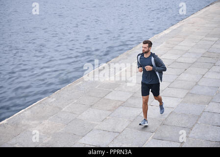 Sérieux au sujet de rester en forme. Vue de dessus du jeune homme dans les vêtements de sport jogging lors de l'exercice en plein air Banque D'Images