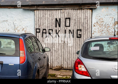 Voitures garées en face d'un No Parking sign peint sur une porte de garage à Schull, West Cork, Irlande. Banque D'Images