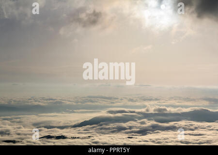 Large fantastique vue de dessus de la vallée de montagne rempli de puffy blanc comme neige les nuages et le brouillard qui s'étend à l'horizon lumineux sous le ciel nuageux du matin au d Banque D'Images