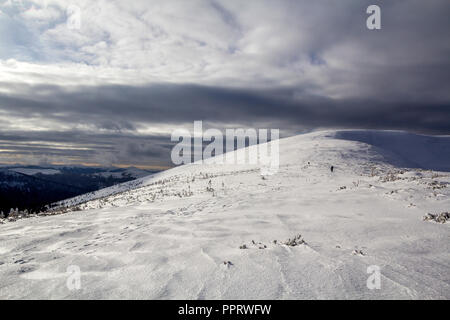 Paysage de montagne d'hiver. Large Vue sur montagne couverte de neige brillante et petites silhouettes d'voyageurs randonneurs sous ciel nuageux bleu foncé stor Banque D'Images