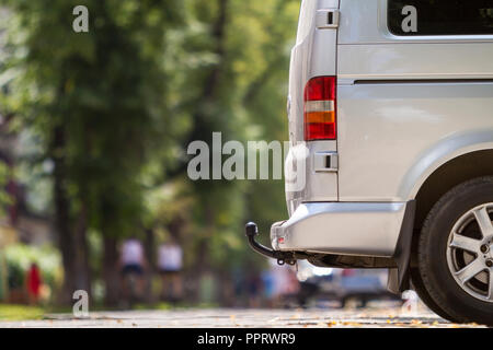 Close-up Vue de côté détail d'argent taille moyenne passager minibus de luxe van avec œillet de barre en stationnement sur la chaussée, rue de la ville ensoleillée d'été brouillée avec sil Banque D'Images